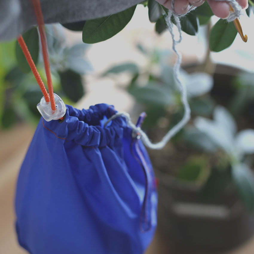 青い巾着袋に入れたモバイル編みセット。外出先でかぎ針編みを楽しむための持ち出しグッズのイメージ。