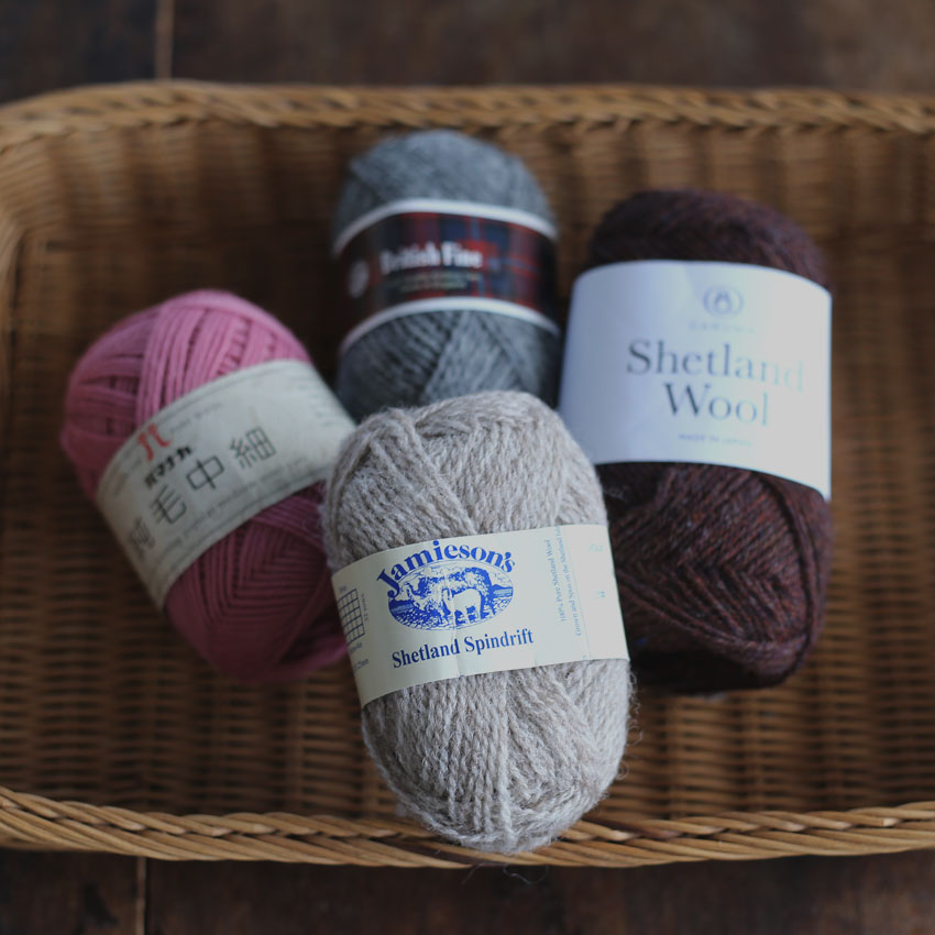 カゴの中に並んだ異なる種類の毛糸玉。代用できる太さの近い糸を探すための比較イメージ。