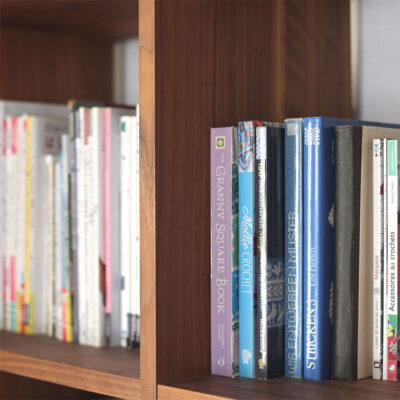 本棚に並ぶたくさんの洋書。かぎ針編みの英文パターンを読み解き、海外のデザインを楽しむイメージ。