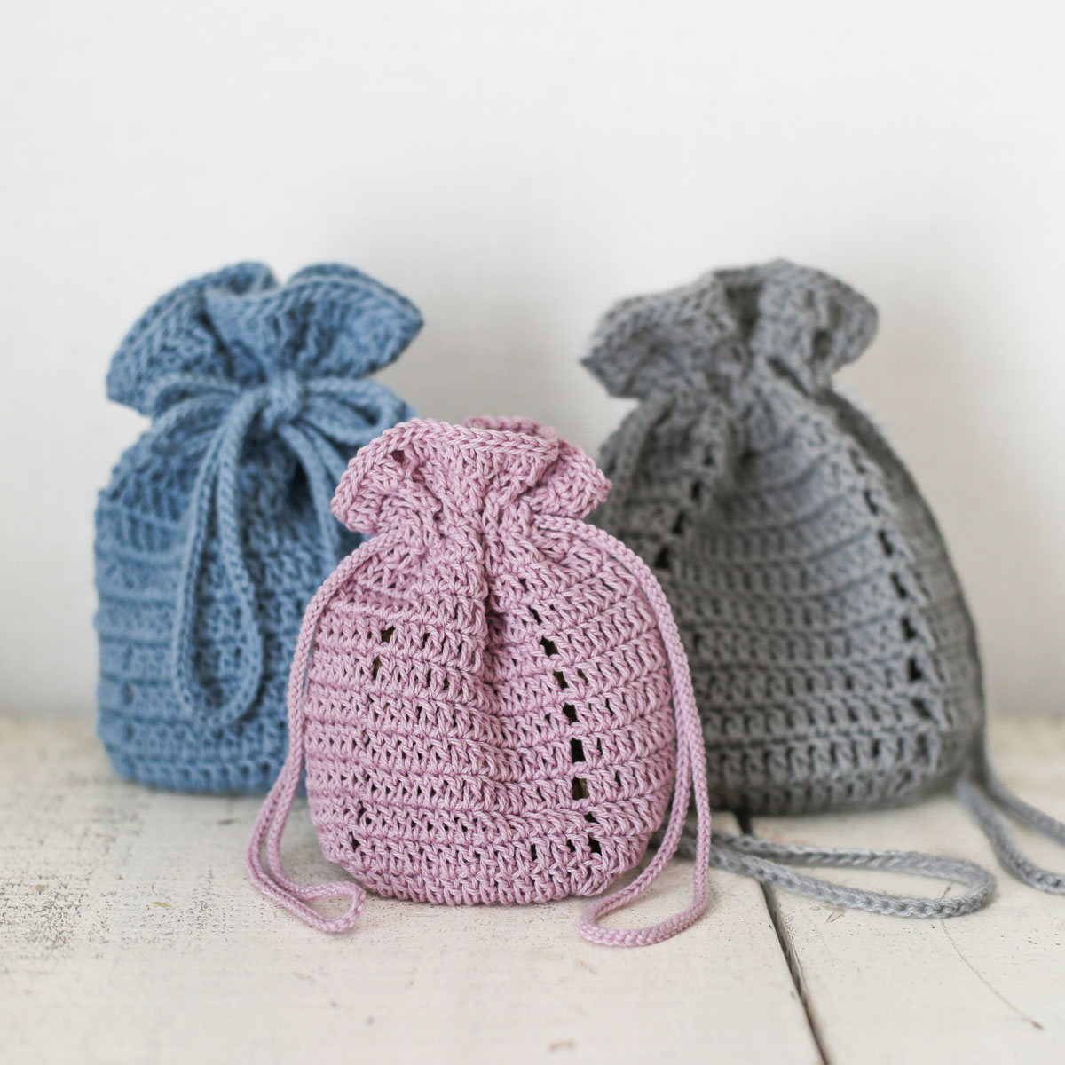 定番小物からはじめる かぎ針編み初心者コース［第2回］。長編みの丸底巾着。ブルー、ピンク、グレーの3色が明るい白背景で並んでいる様子。