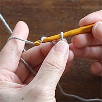 スレッドコードの編み方［2］ループの根元を押さえ、針に糸をかけてループにくぐらせます。
