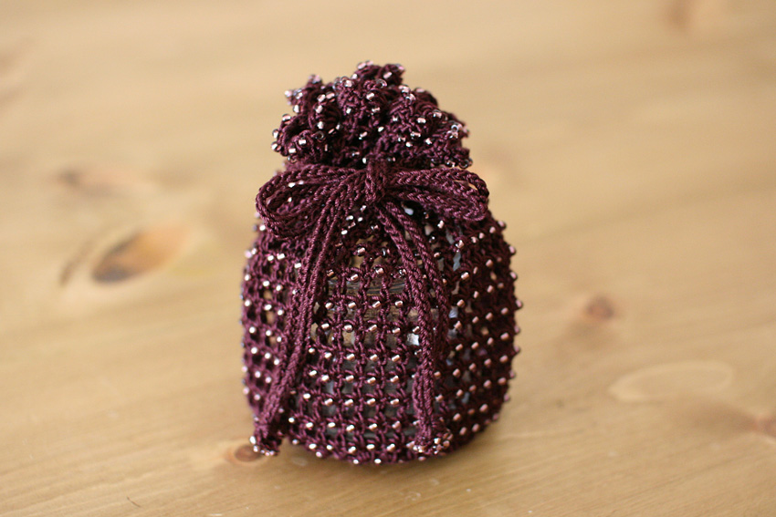 ビーズ編みの技法を応用して作られた巾着袋。かぎ針編みの編み地全体にビーズが散りばめられた小物づくりの例。