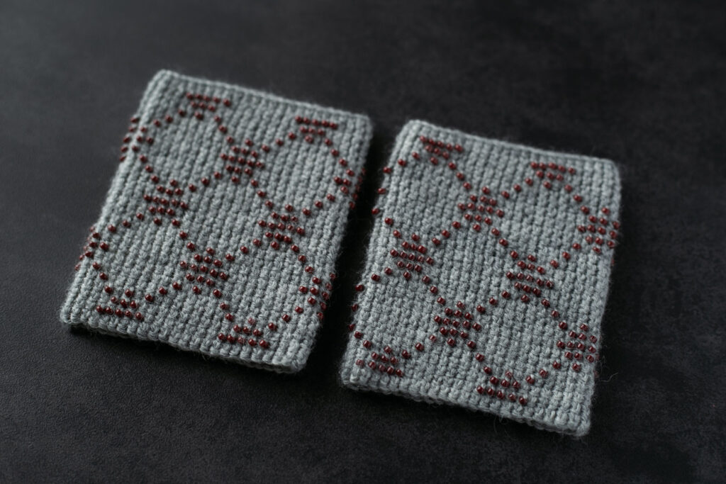 かぎ針編みの編み目とビーズが整然と並ぶクロップアップ写真。編み地の質感とビーズの輝きの詳細。