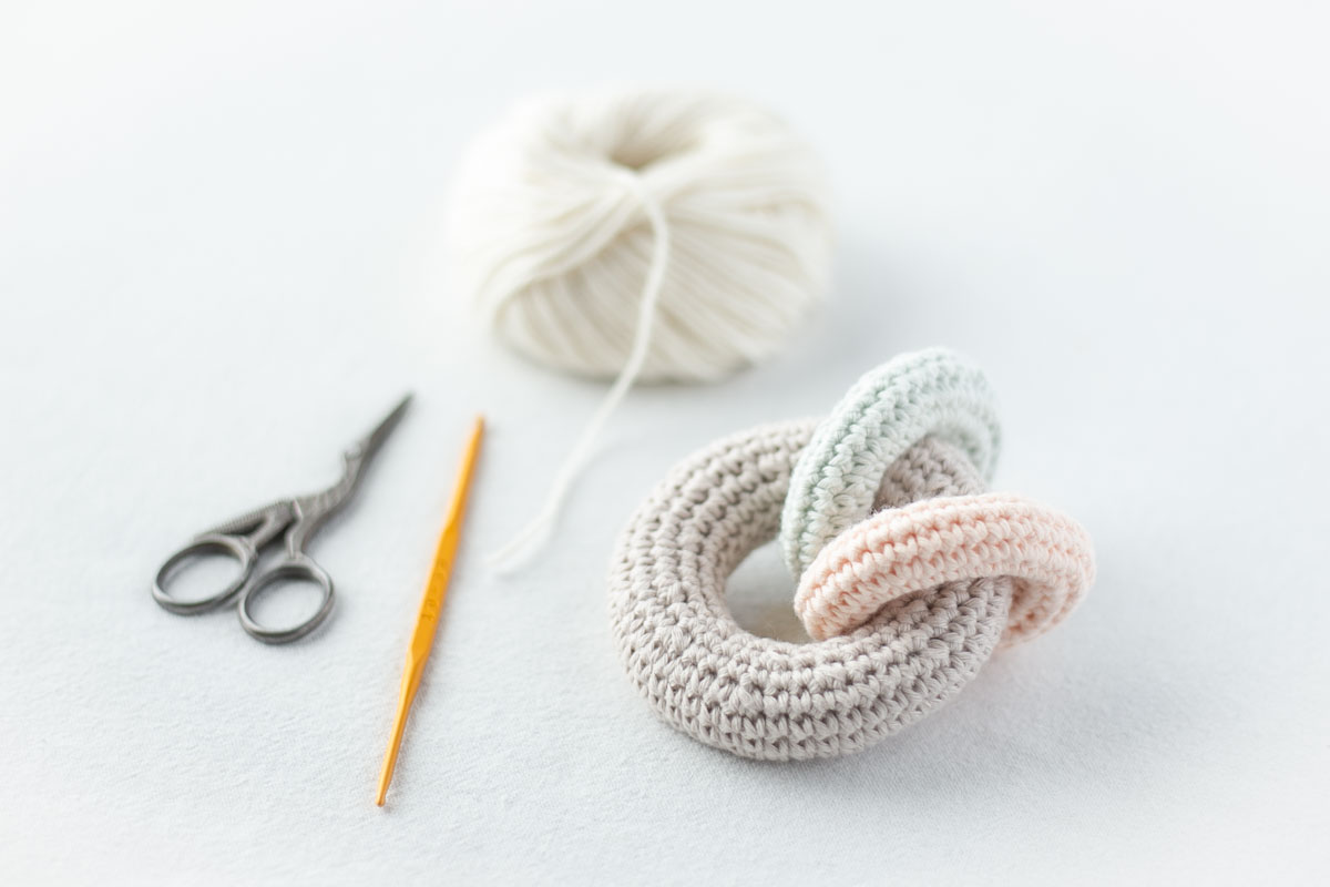 かぎ針編みのベビーラトル（赤ちゃんのガラガラ）。かぎ針、ハサミとともに、編みかけの風景。